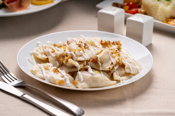 Dumplings with fried onions on white plate, pouring sour cream. Varenyky, vareniki ukrainian national cuisine