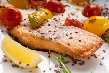 Fried salmon fillet with lemon and vegetables served on white plate on table