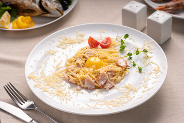 Pasta Carbonara on white plate with parmesan and yolk serving on table in restaurant or cafe