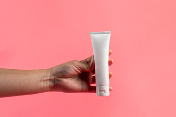 Hand and plastic white tube for cream or lotion. Skin care or sunscreen cosmetic on pink background.