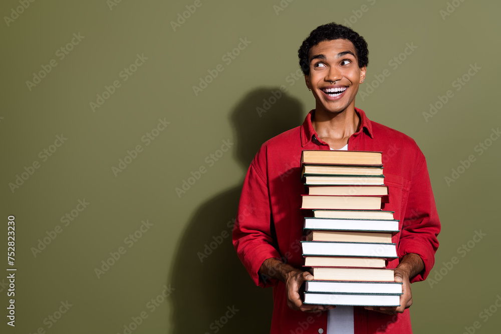 Poster Photo of funny cheerful man dressed red shirt carrying big heavy book pile looking empty space isolated green color background