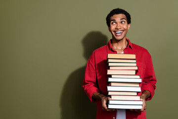Photo of funny cheerful man dressed red shirt carrying big heavy book pile looking empty space isolated green color background