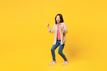 Full body young woman of Asian ethnicity wear pink t-shirt beige shirt pastel casual clothes do winner gesture celebrate clenching fists say yes isolated on plain yellow background Lifestyle portrait