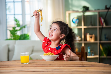 Indian happy little girl eat pasta spaghetti or noodles in a bowl at home