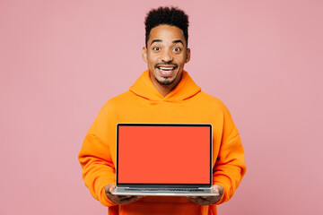 Young surprised IT man of African American ethnicity wear yellow hoody casual clothes work hold use blank screen workspace area laptop pc computer isolated on plain pink background. Lifestyle concept.
