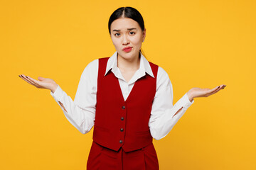 Young corporate lawyer employee business woman of Asian ethnicity wear formal red vest shirt work at office shrugging shoulders spread hands isolated on plain yellow background studio. Career concept.