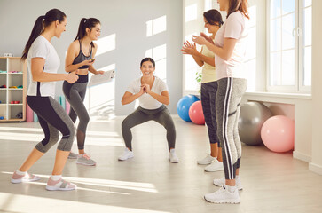 In the gym, a group of smiling women actively participate in squat exercises, smiling and providing support to mate throughout the workout. Teamwork and camaraderie during active exercise session.