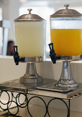 In the dining room two large beverage dispensers stand on a sturdy metal stand. One dispenser holds...