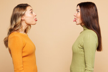 Side view young friends two women they wear orange green shirt casual clothes together look to each...