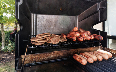 Sausages and hamburger patties have been cooked on the BBQ and are staying warm on the shelf while others cook.