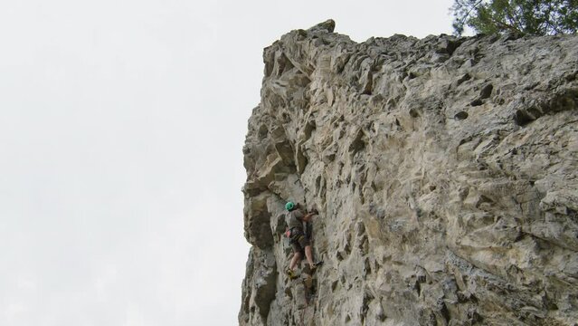 View from below of man climbing steep rock with rope while doing extreme sports in nature on summer dayView from below of man climbing steep rock with rope while doing extreme sports in nature on summ