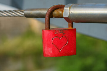 Love lock with carved heart hanging on the metal railing on the bridge. Green blurred background....