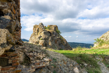 Fototapeta na wymiar On the top of Kojori fortress. Ruins of the wall and tower made from rock and bricks. Landscape of nearby mountains and villages. Clear blue sky and clouds. Georgia.