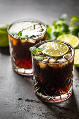 Tropical alcoholic cocktail Cuba Libre composed of white rum, cola, ice cubes, lime and mint - obrazy, fototapety, plakaty