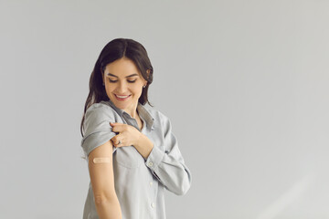 Happy smiling young lady showing arm after flu or Covid-19 vaccine injection. Woman promoting...