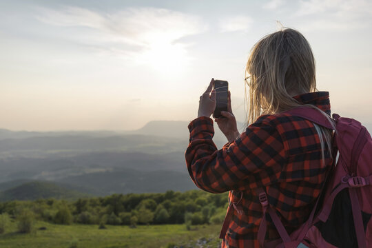 Adolescent girl taking photos of fantastic mountain landscape at sunset with smartphone