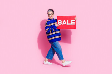 Full size photo of pretty retired female walk hold shopper sale plate dressed stylish blue striped outfit isolated on pink color background