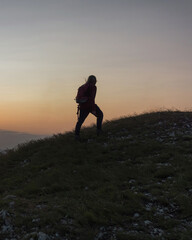 Female hiker silhouette with a backpack walking and following the trail uphill, enjoying the sky at...