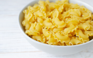 Raw Creste Di Gallo pasta in a gray bowl on a white wooden board. Rooster comb. The concept of traditional Italian food. Horizontal orientation. Copy space. Selective focus