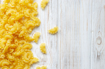 Raw Creste Di Gallo pasta scattered in a heap on a white wooden board. Rooster comb. The concept of traditional Italian food. Horizontal orientation. Copy space. Selective focus. Top view