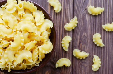 Raw Creste Di Gallo pasta in a ceramic bowl on a brown wooden board. Rooster comb. The concept of...