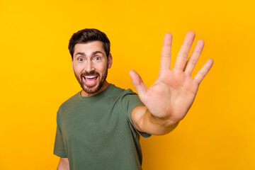 Photo of positive cheerful guy dressed green t-shirt waving arm palm hi isolated yellow color...