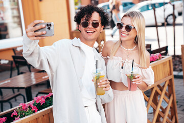 Young smiling beautiful woman and her handsome boyfriend in casual summer clothes. Happy cheerful family. Female having fun. Couple posing in street. Holding and drinking cocktail drink in plastic cup