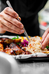 close-up view of hands garnishing grilled meat on a plate. The hands, holding tweezers,...