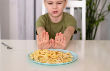 Poor little boy refuses to eat. An upset child sits in kitchen at table without an appetite and...