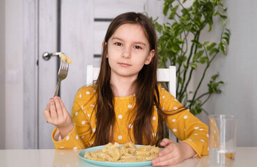 Happy girl eating pasta. Child eats his lunch in kitchen at table. Selective focus