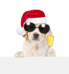 Cute Golden retriever puppy wearing sunglasses and santa hat looks above empty white banner and...