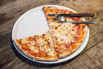 Pizza background. Pizza on white plate on wooden table. Knife and fork. Margherita pizza. Simple and delicious dinner. Rustic style food. One piece missing.