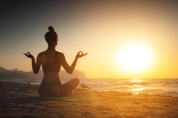 Yoga woman meditating at serene sunset or sunrise on the beach. The girl relaxes in the lotus position. Fingers folded in mudras.