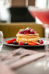 Homemade fluffy pancake with fruits and cream on the top, on a coffee shop table. Side view