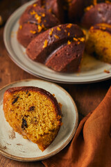 Delicious homemade pumpkin bundt cake with prunes and sherry, decorated with frosting and zest on a wooden background.