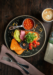 English Breakfast served on a black ceramic plate. Wooden table. Top view