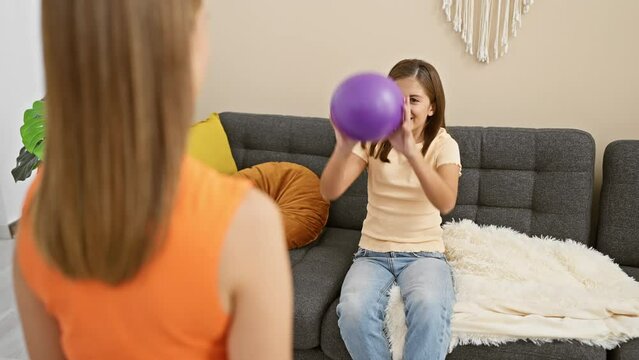 Mother and daughter enjoy playful interaction with a ball in a cozy living room, depicting family bonding and happiness.