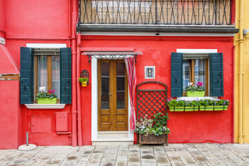 Murano and Burano island landscape. Venice region in Italy. Colorful various home facades. Red paint house. Decorative flower plant pots and color paint window shutters. Italian architecture.