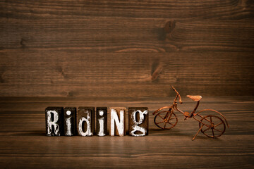 RIDING. Text from alphabet blocks and rusty miniature bicycle on wood texture background