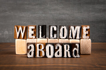 WELCOME ABOARD Concept. Alphabet blocks on wood and blackboard background