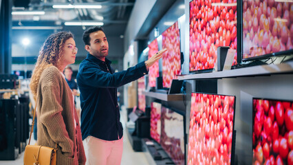 Stylish Multiethnic Couple is TV Shopping at Retail Electronics Store. Man and Female Seeking Sleek...