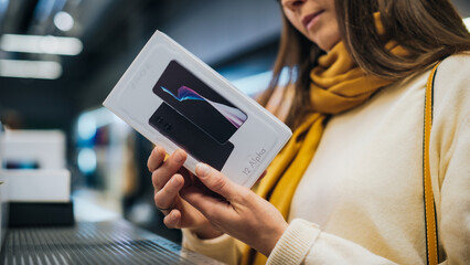 Close Up Portrait of a Stylish Woman Looking at a Box with Modern Smartphone, Reading Model's Specifications and Features. Client Shopping for a New Mobile Phone in a Home Electronics Store