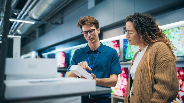 Portrait of a Female Customer Seeking Advice from Retail Home Electronics Expert. Hispanic Girl Explores Smartphone Options. Shopper Evaluating Latest Mobile Phone Innovations in a Department Store
