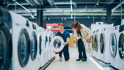 Middle-Aged Woman Interacts with Home Electronics Store Consultant During Washing Machine Selection. Senior Customer Explores Laundry Appliance Options. Shopper in Modern Retail Shop - obrazy, fototapety, plakaty