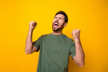 Photo of excited funky man wear khaki t-shirt closed eyes shouting yes rising fists isolated yellow...