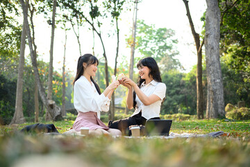 Young woman friends sitting on grass and eating sandwiches during picnic in par