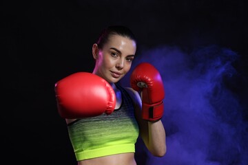 Portrait of beautiful woman wearing boxing gloves in color lights and smoke on black background