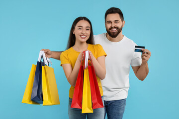 Happy couple with shopping bags and credit card on light blue background