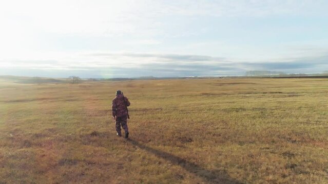 A hunter with a gun walks across a field in autumn