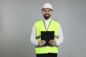Engineer in hard hat holding clipboard on grey background